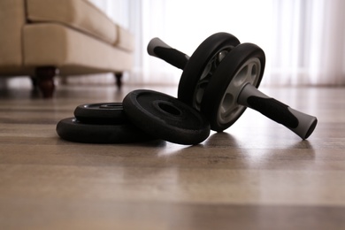 Photo of Abs roller and weight plates on floor in room. Home fitness