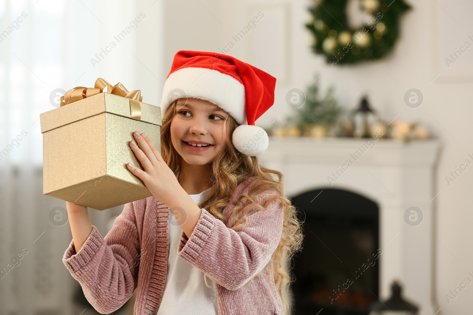 Photo of Happy little girl with Christmas gift near fireplace at home. Space for text