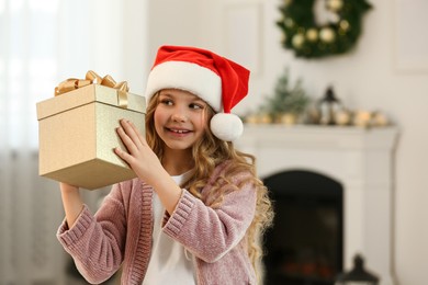 Happy little girl with Christmas gift near fireplace at home. Space for text