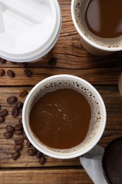 Photo of Coffee to go. Paper cups with tasty drink and beans on wooden table, flat lay