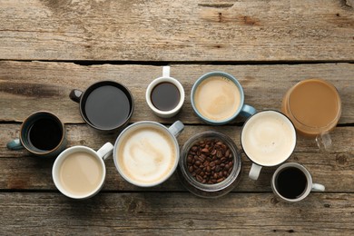 Different coffee drinks in cups and beans on wooden table, flat lay