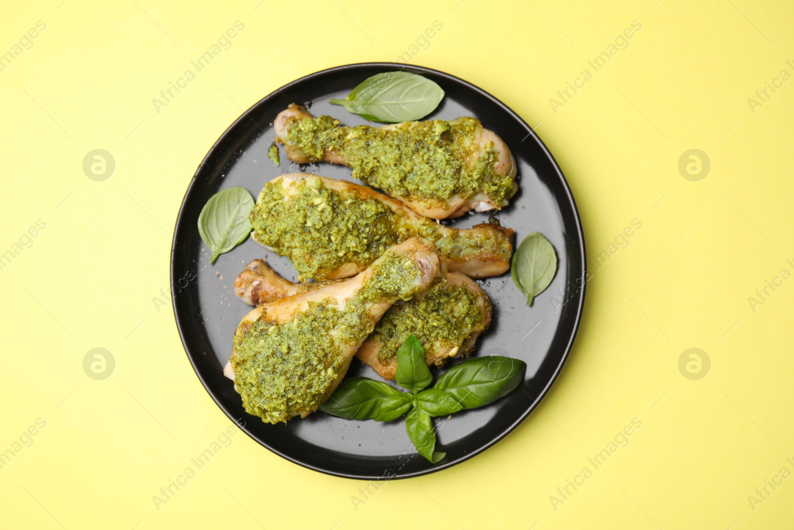 Photo of Delicious fried chicken drumsticks with pesto sauce and basil on yellow table, top view