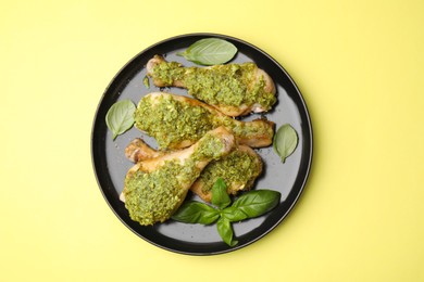 Photo of Delicious fried chicken drumsticks with pesto sauce and basil on yellow table, top view