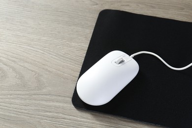 Photo of Wired mouse and mousepad on wooden table, space for text