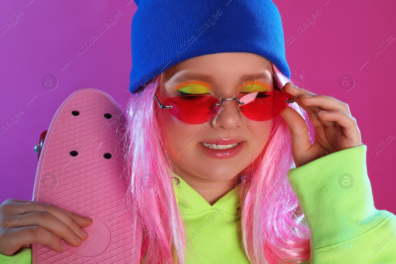 Photo of Cute indie girl with penny board on violet background