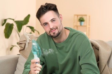 Photo of Sick man holding nebulizer for inhalation indoors