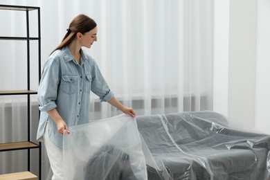 Photo of Young woman putting plastic film away from sofa at home