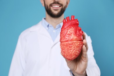 Photo of Doctor with model of heart on light blue background, closeup. Cardiology concept