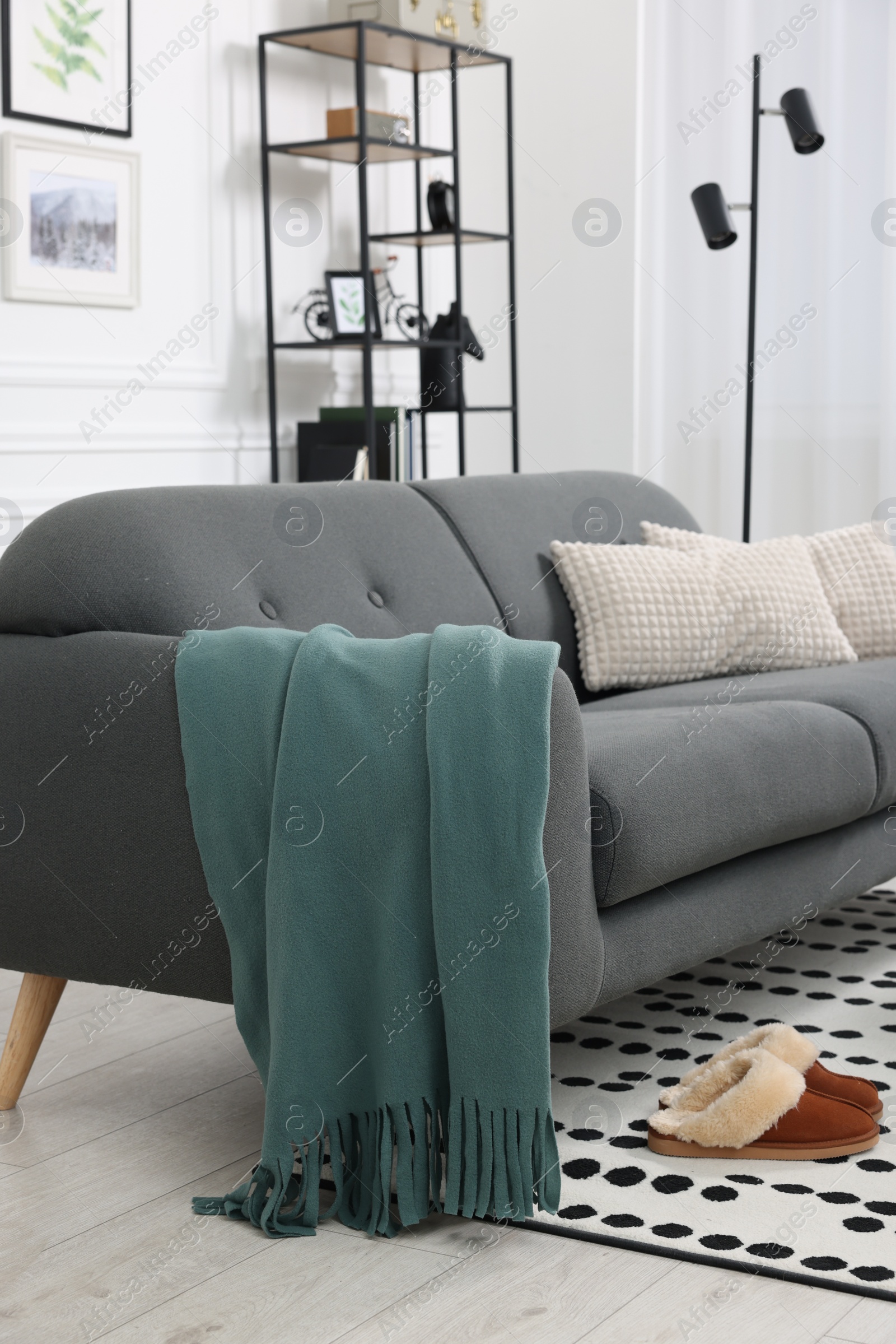 Photo of Comfortable sofa with green blanket, pillows and slippers in living room