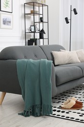 Photo of Comfortable sofa with green blanket, pillows and slippers in living room