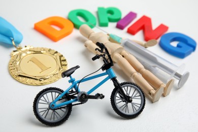 Word Doping, syringe, medal, sportsman and bicycle model on white table