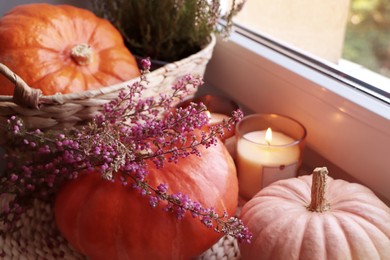 Wicker basket with beautiful heather flowers, pumpkins and burning candles near window indoors, closeup