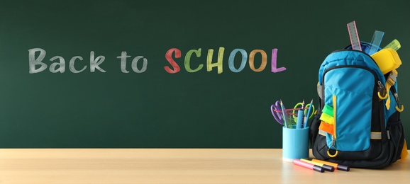 Backpack and different stationery on wooden table near green chalkboard with text Back To School. Banner design 