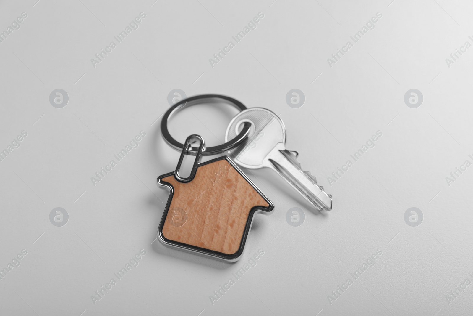 Photo of Key with trinket in shape of house on white background, above view. Real estate agent services