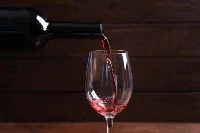 Photo of Pouring delicious red wine into glass on blurred background