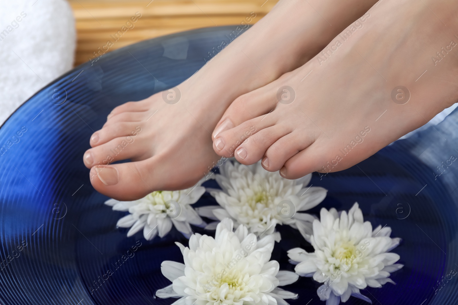 Photo of Woman holding her feet over bowl with water and flowers, closeup. Spa treatment