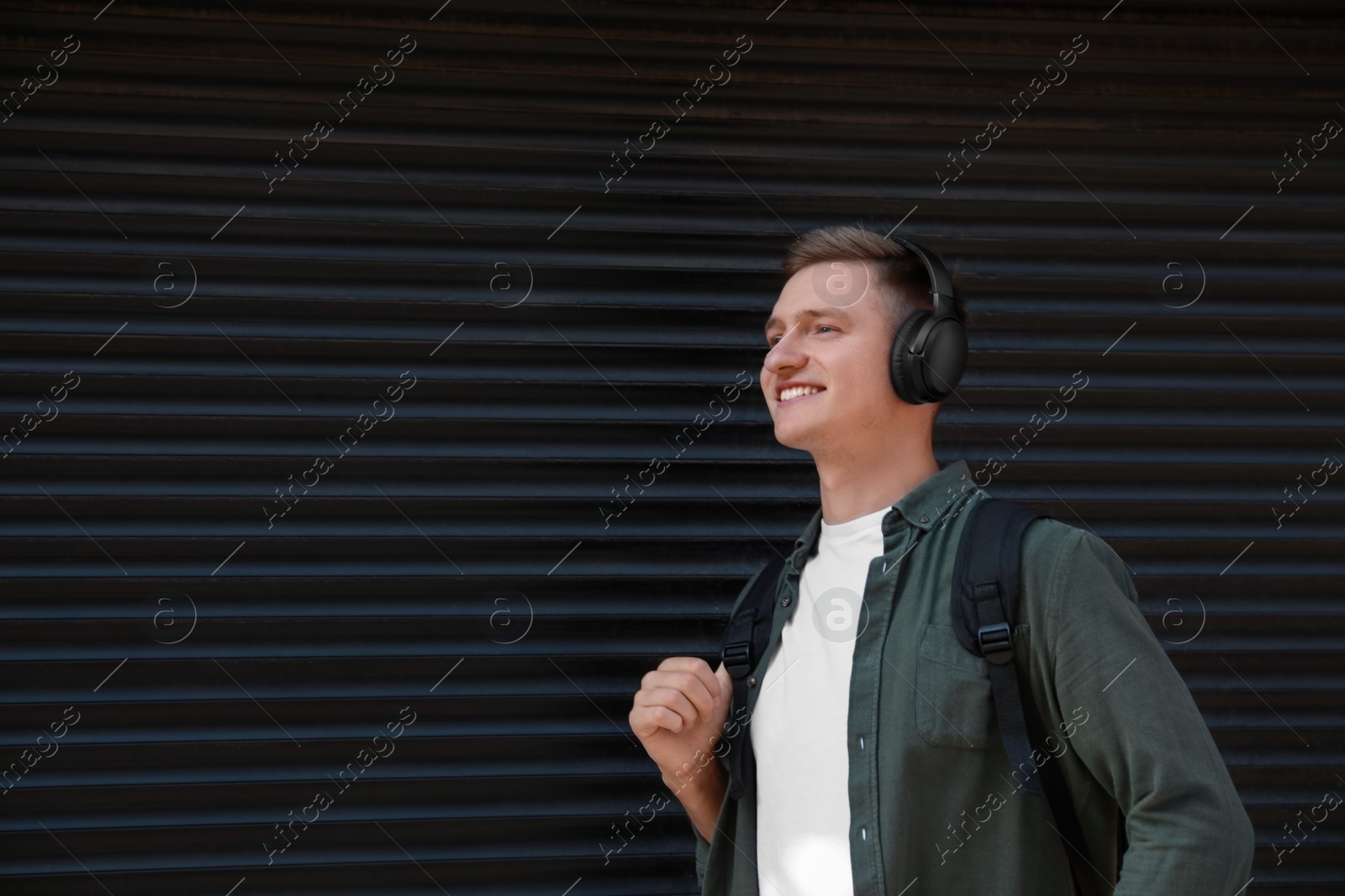 Photo of Smiling man wearing headphones near shutters outdoors. Space for text