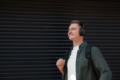 Photo of Smiling man wearing headphones near shutters outdoors. Space for text