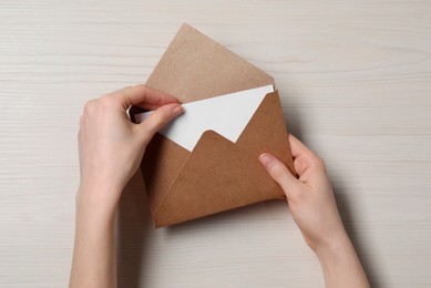 Photo of Woman taking card out of letter envelope at light wooden table, top view