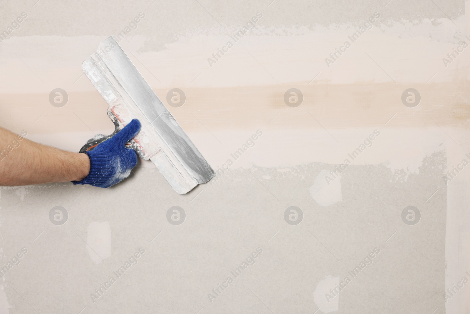 Photo of Worker plastering wall with putty knife indoors, closeup. Space for text