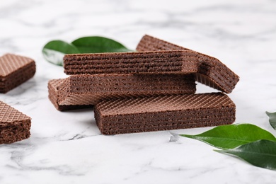 Delicious chocolate wafers with leaves on marble background