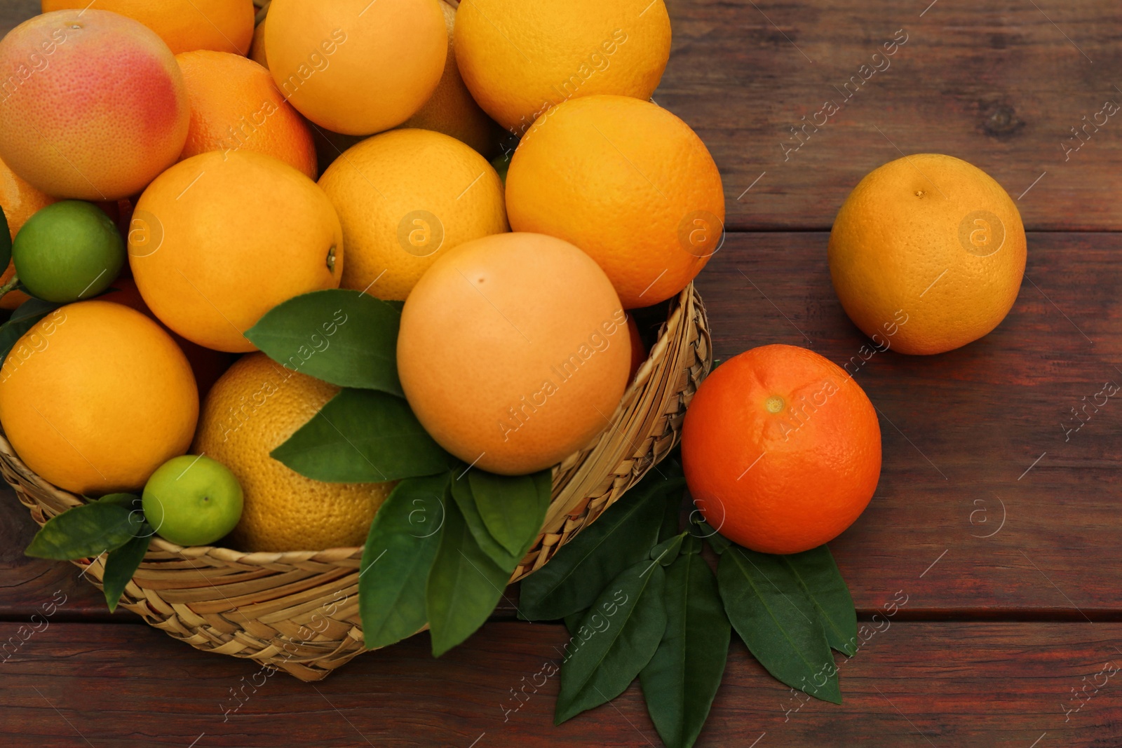 Photo of Wicker basket with different citrus fruits and leaves on wooden table, closeup