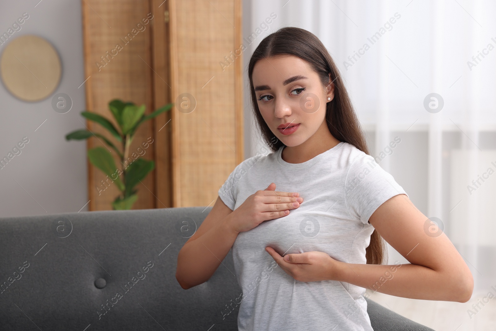 Photo of Beautiful young woman doing breast self-examination at home, space for text