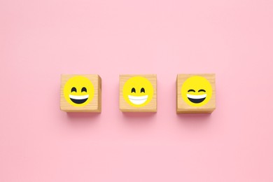 Wooden cubes with different emoticons on pink background, flat lay