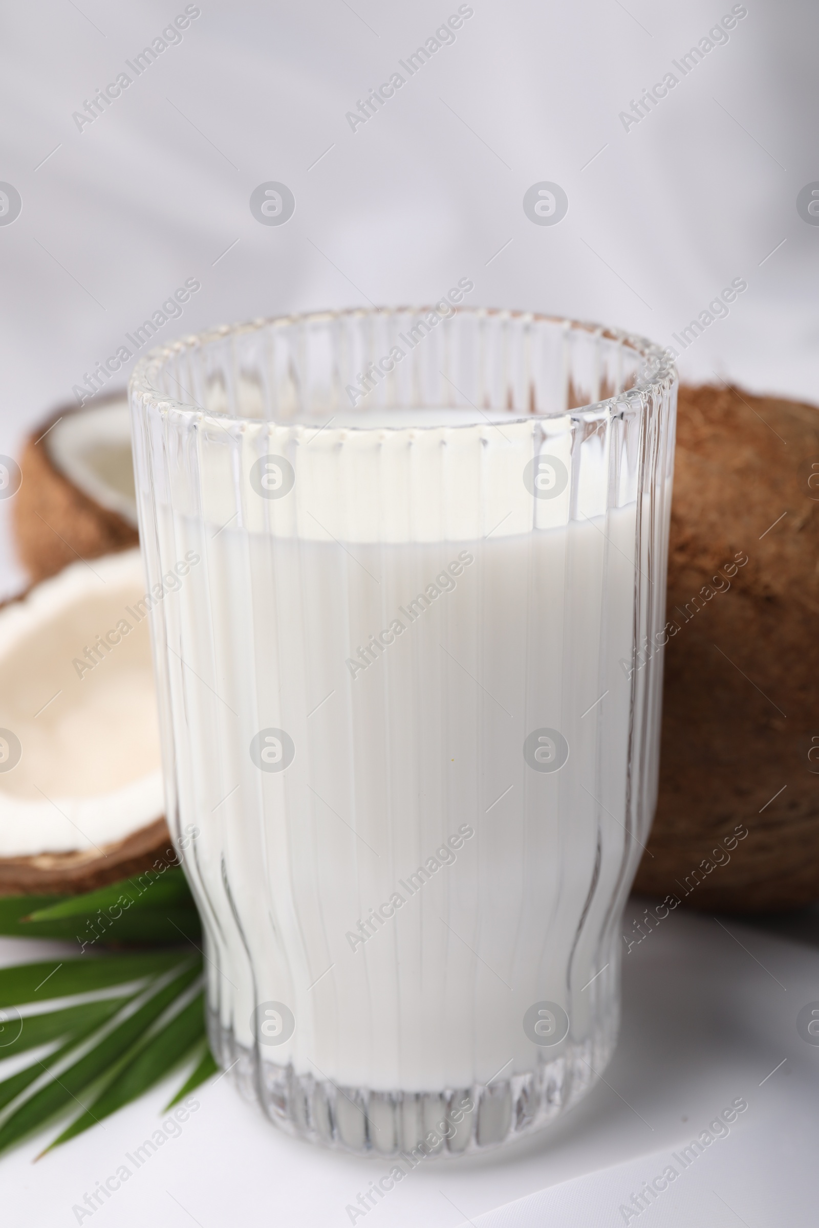 Photo of Glass of delicious coconut milk, palm leaves and coconuts on white table