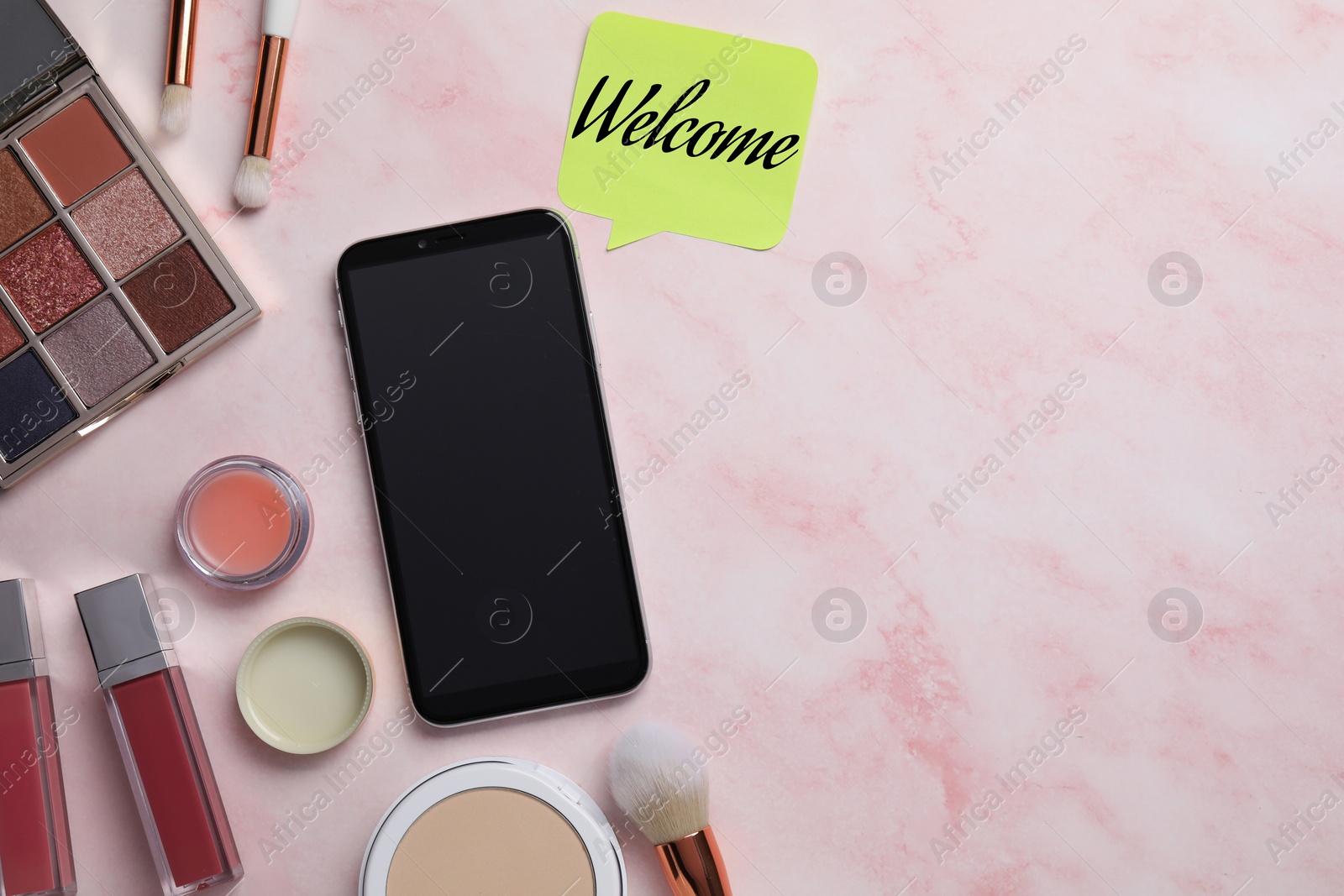 Image of Sticky note with word Welcome near smartphone and makeup products on pink table, flat lay