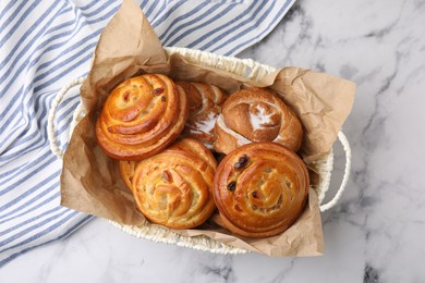 Delicious rolls with raisins and sugar powder in basket on white marble table, top view. Sweet buns