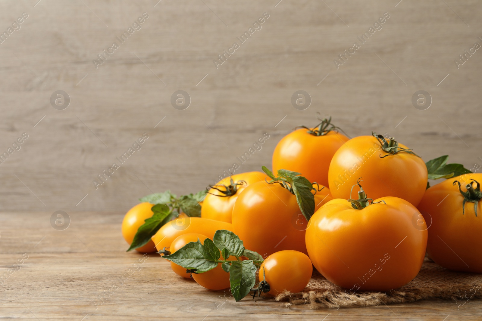 Photo of Fresh ripe yellow tomatoes with leaves on wooden table. Space for text