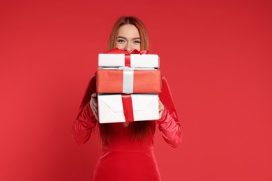 Young woman with Christmas gifts on red background
