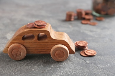 Wooden car model and coins on grey background