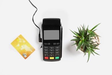 Modern payment terminal, plant and credit card on white background, top view