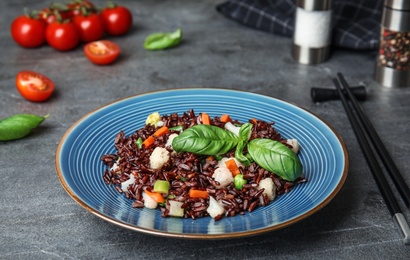 Photo of Plate of brown rice with vegetables on grey table