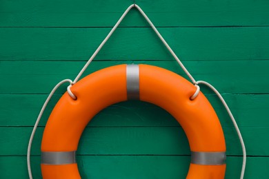 Photo of Orange lifebuoy hanging on green wooden wall. Rescue equipment