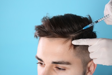 Young man with hair loss problem receiving injection on color background, closeup