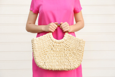 Young woman with stylish straw bag near white wall, closeup