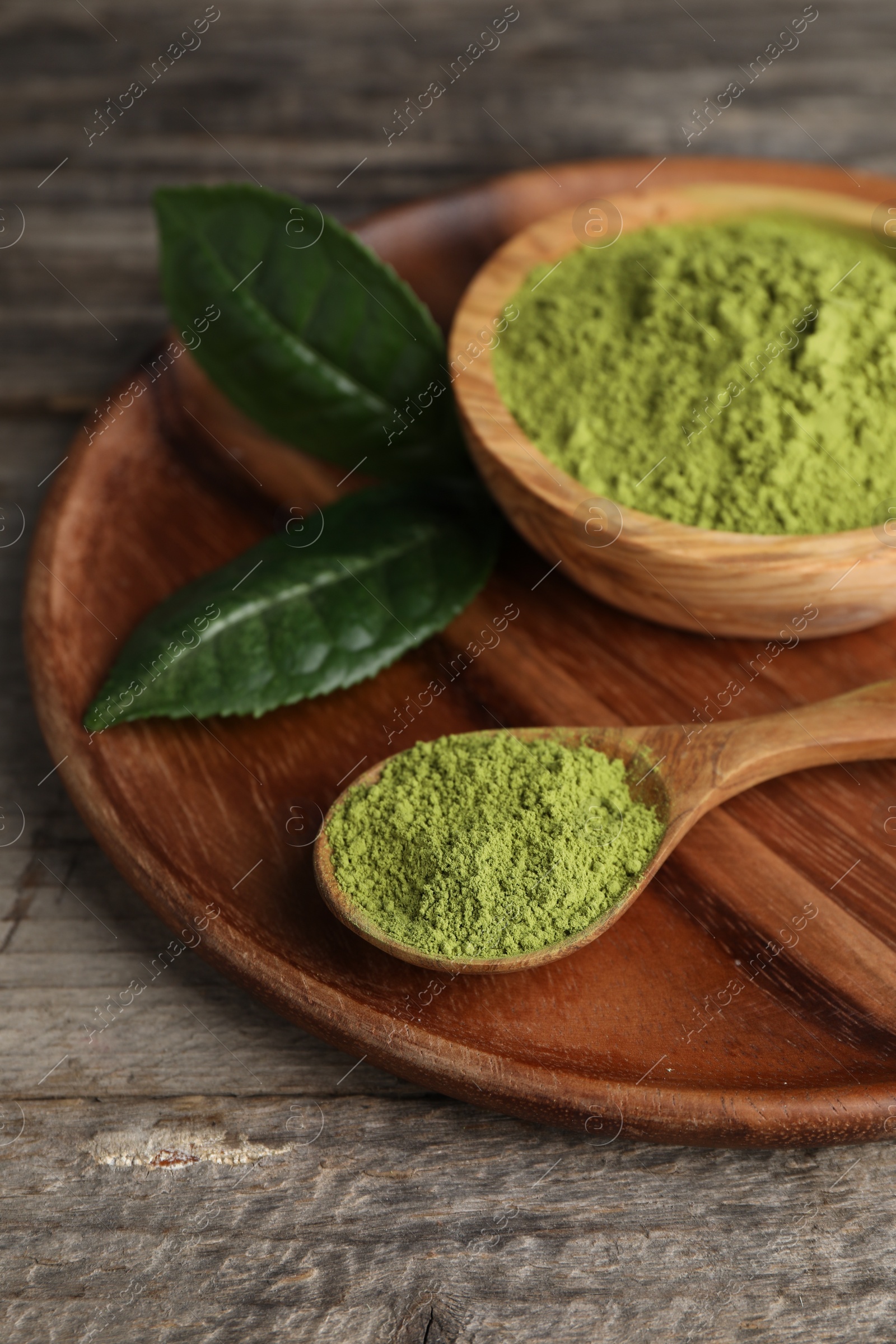 Photo of Spoon and bowl with green matcha powder on wooden table, closeup