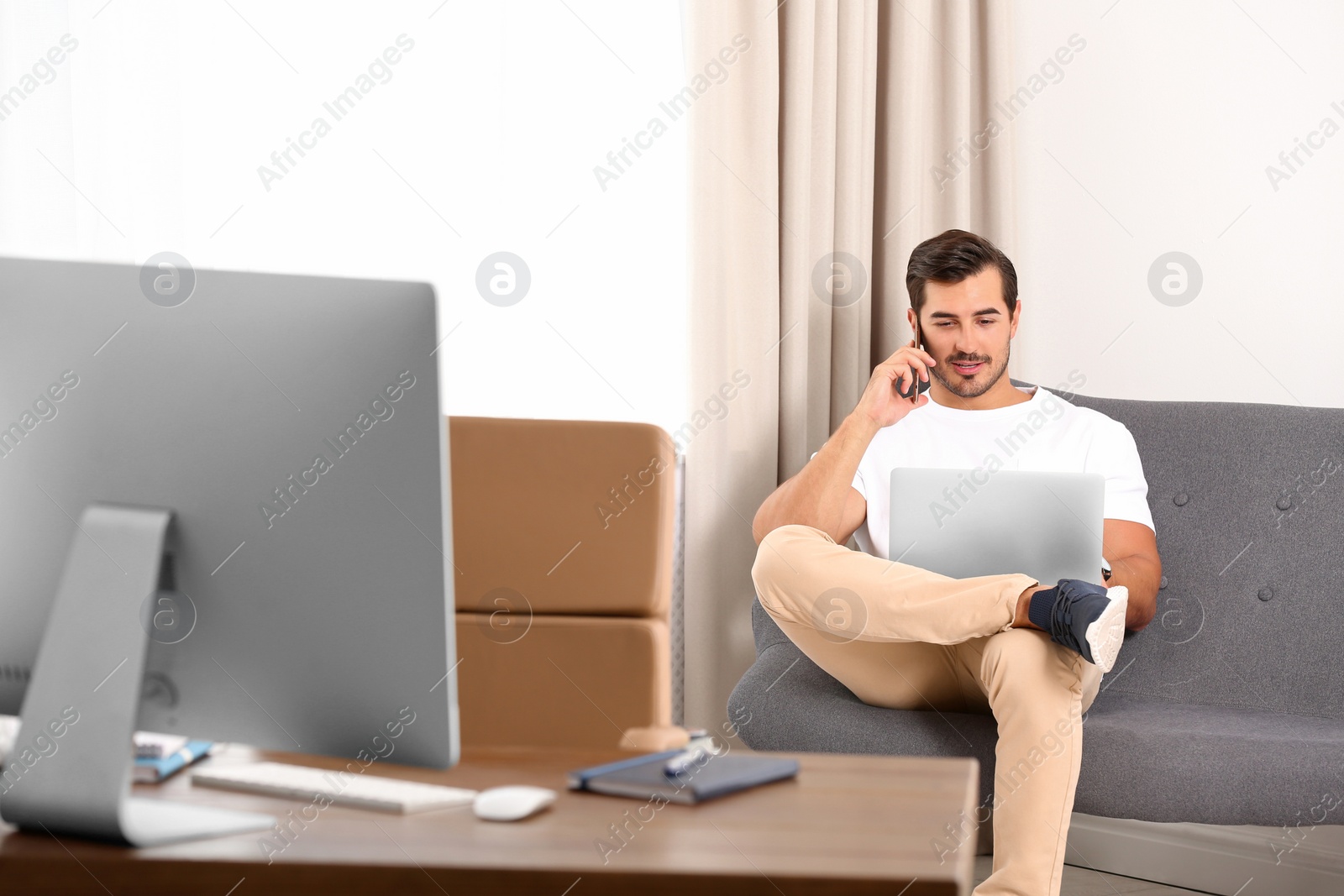 Photo of Handsome young man talking on phone while working with laptop indoors