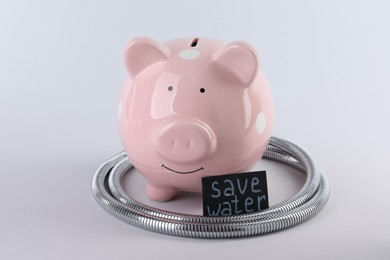 Photo of Water scarcity concept. Card with phrase Save Water, piggy bank and shower hose isolated on white