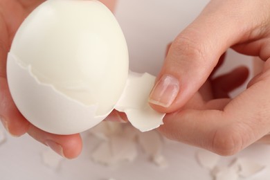 Photo of Woman peeling boiled egg at white table, closeup