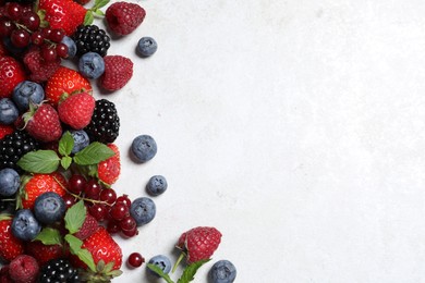 Many different fresh ripe berries on white textured table, flat lay. Space for text