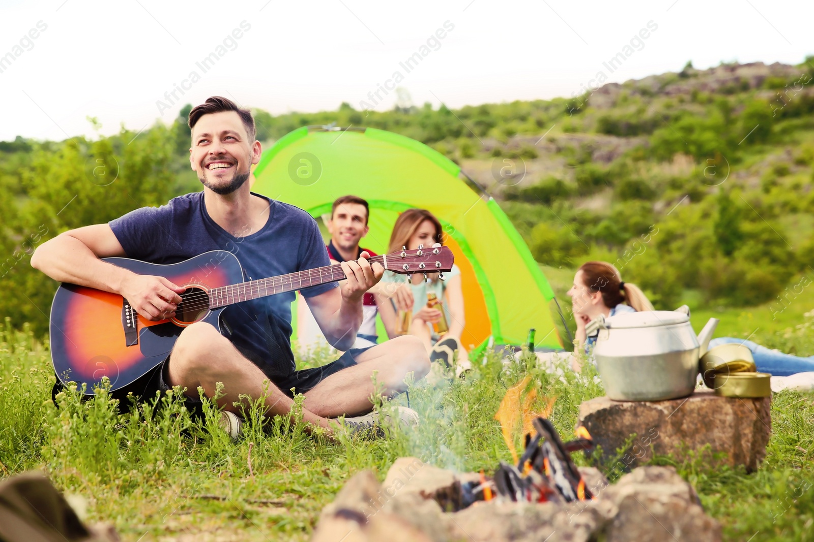 Photo of Man playing guitar near camping tent in wilderness