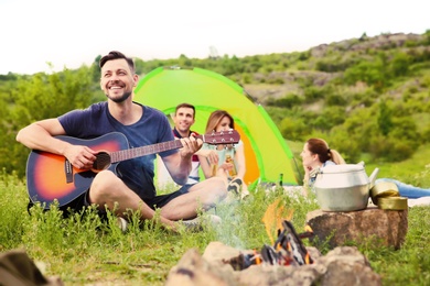 Photo of Man playing guitar near camping tent in wilderness