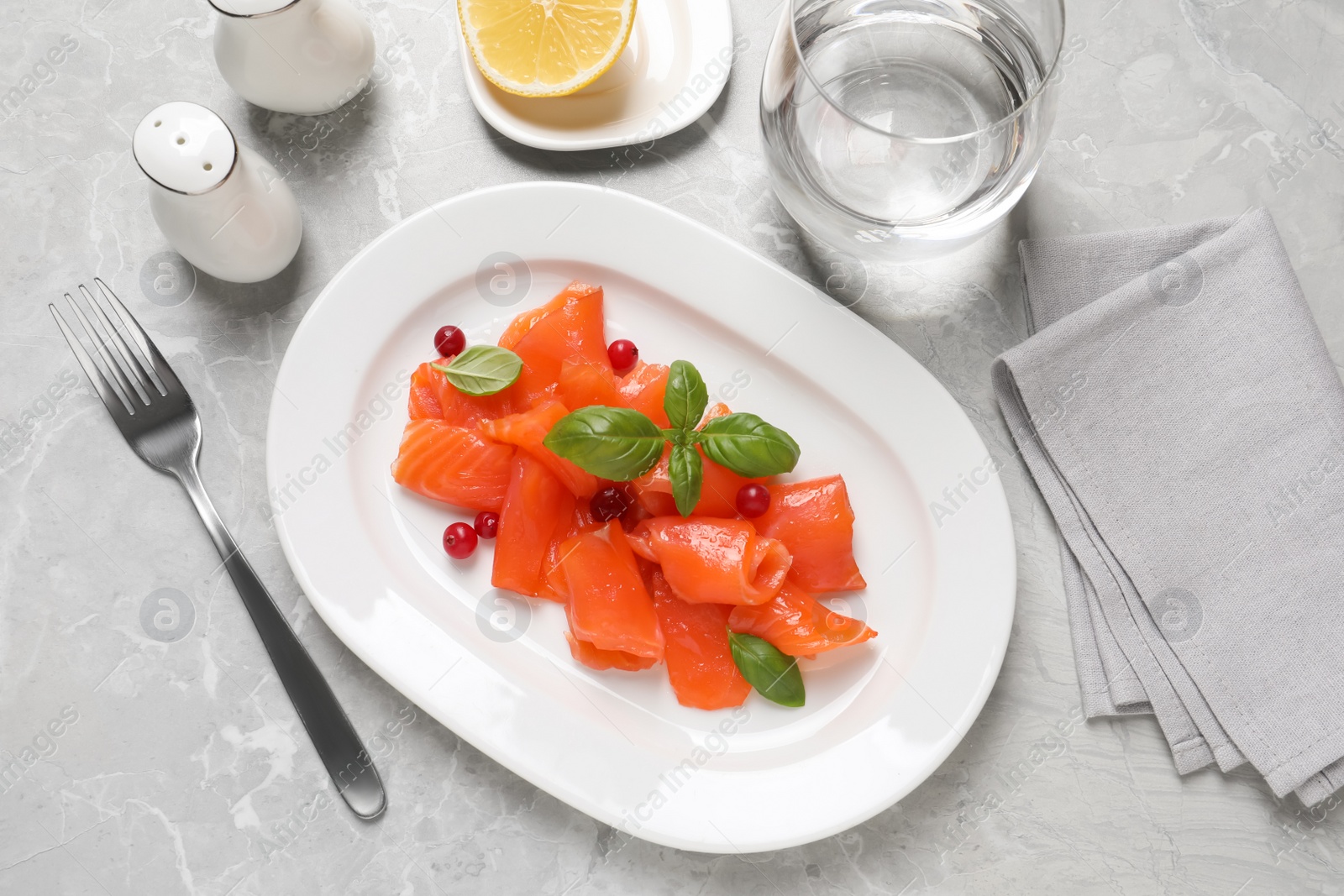 Photo of Salmon carpaccio with cranberries and basil served on grey table, flat lay