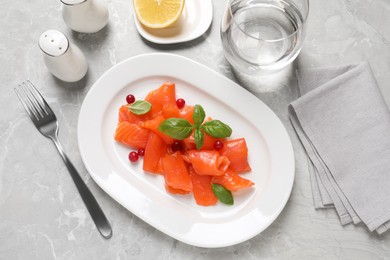 Salmon carpaccio with cranberries and basil served on grey table, flat lay