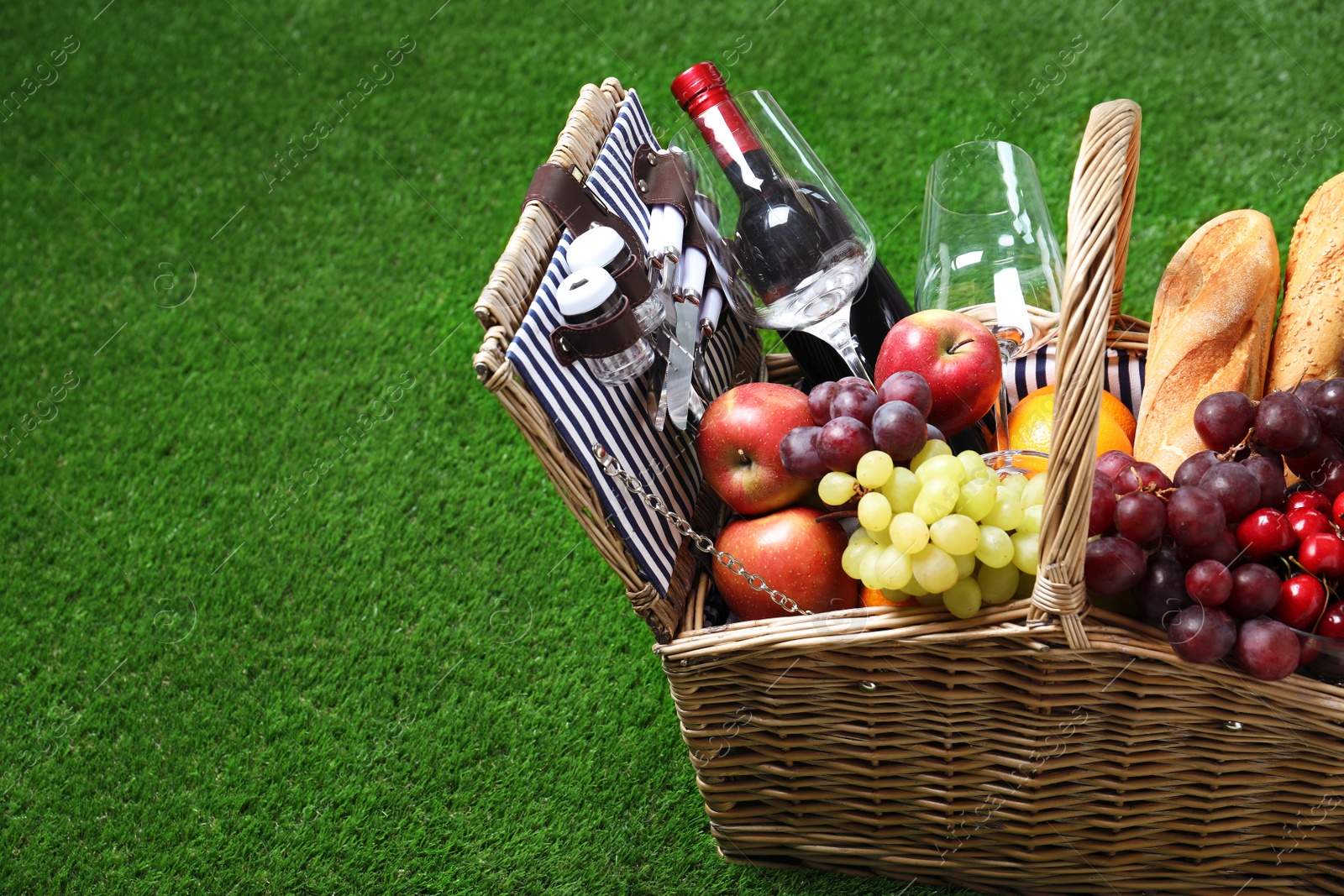 Photo of Wicker picnic basket with different products on green grass, space for text