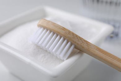 Bamboo toothbrush and bowl of baking soda on white table, closeup